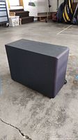 Lateral view of the rectangular black Onkyo subwoofer placed on a concrete floor showing general condition and side panel.