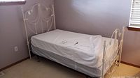 Side view of painted iron twin bed frame with mattress in room, showing full length and part of headboard and footboard.