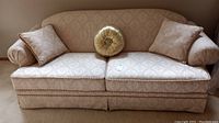 Full front view of the damask patterned ivory gold sofa with pillows and loose seat cushions