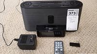 Front view of the Sony black clock radio with iPod dock, showing the display and docking port with adapter, remote, and power adapter beside it.