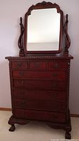 Front view of a tall solid mahogany dresser with seven drawers and attached tilting mirror, featuring ornate carvings and swing-handled drawer pulls.