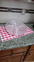 Clear plastic revolving appetizer tray with vented compartments and central spindle shown on granite counter with red and white checkered cloth under it.