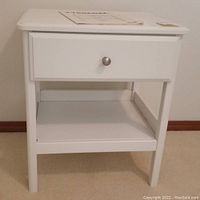 Front view of white IKEA nightstand showing drawer with metal knob and open shelf below