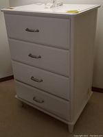 Front view of white chest with four drawers and metal handles.