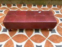 Red leather tufted rectangular bench on patterned rug, clear front view.
