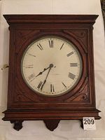 Front view of antique Seth Thomas wall clock, showing wood case with carved detailing and worn metal clock face with Roman numerals.