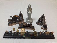 Overview of six Asian-themed figurines and decorative pieces including silver-toned statue, pagodas, Buddha, ox, train, and incense holder.