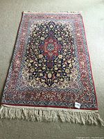 Full view of rug laid out on carpet showing total dimensions, design and fringes
