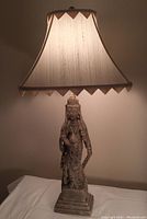 Fully assembled plaster table lamp with indigenous person figure and decorative fabric shade turned on to show lighting function.