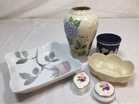 Collection overview showing Rosenthal tray with pink floral design, Lenox vase with hydrangea motif, Wedgwood blue jasperware cup, Belleek cream bowl, and two small Aynsley trinket boxes with floral patterns