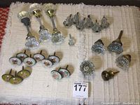 Overview of door knobs and floral pulls on a beige textured cloth, featuring clear glass and floral decorative pulls with screws