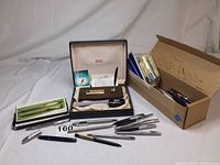 Full lot overview showing boxed Cross desk set, several boxed pens, brown cardboard box holding additional pens and refills