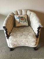 Front angle of the vintage club chair showing cream upholstery with leaf pattern fabric, carved dark cherry stained wood paw feet, and included elephant embroidered silk pillow.