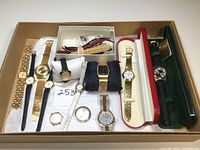 Full view of the lot with multiple watches in gold-tone, some with leather bands, arranged in a box with extra bands in a small compartment