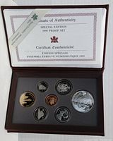 Open brown display case showing seven proof coins arranged in a foam insert with a Certificate of Authenticity on the lid