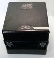Closed black metal carrying case with caution label on top noting precision instrument and instructions for careful handling