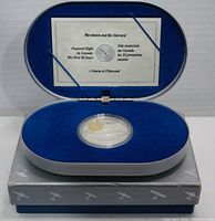 Photo showing the 1990 Royal Canadian Mint 20-dollar coin in a clear protective capsule, set in a blue velvet-lined presentation box with labeled lid, placed on a gray outer box with airplane silhouettes.