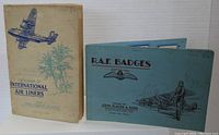 Two cigarette card albums displayed closed: one blue 'R.A.F. Badges' album with aircraft and pilot illustration, and one cream-colored 'International Air Liners' album with airplane and palm tree artwork.
