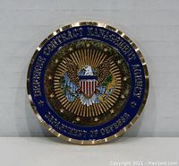 Front side of the challenge coin showing the eagle emblem with sunburst rays and blue enamel border with gold text 'DEFENSE CONTRACT MANAGEMENT AGENCY DEPARTMENT OF DEFENSE'.