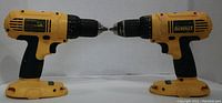 Pair of yellow and black DeWalt cordless drill drivers placed facing each other horizontally showing side profiles