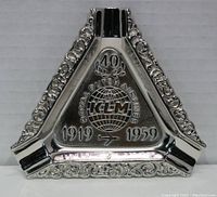 Front view of the triangular silver-toned ashtray with embossed ornate edges featuring KLM logo, dates 1919-1959, and airplane symbol.