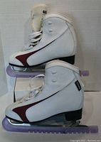 Side view of pair of white soft body ice skates with maroon accent and translucent purple blade guards attached.