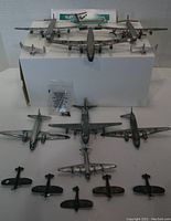 Front top view of 13 die-cast model aircraft on white display box, showing a range of bomber and fighter models and a small plastic bag of parts