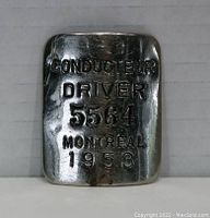 Front view of silver metal badge with engraved text 'CONDUCTEUR DRIVER 5564 MONTREAL 1953'.