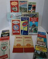 Photo showing multiple vintage road maps and travel guides arranged upright and stacked, including New York, Ontario, Toronto Shell maps, Gulf, Esso, Texaco branded maps, and various provincial and state guides from the 1960s and 1970s.