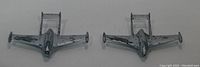 Two silver metal toy planes modeled on the De Havilland Vampire jet aircraft viewed from above on a white background.