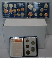 Three UK coin sets displayed: two hard plastic cases with coins from 1966 and 1967, and one soft plastic wallet with additional coins and info card.