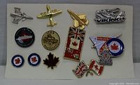 Full view of various military and aviation themed metal pins on white card, showing aircraft, flags, and RCAF insignias.