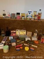 Wide view displaying various vintage apothecary bottles, jars, and boxes arranged on a surface with brown backdrop.