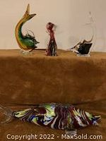 Photo showing three glass fish and one glass dog figurines displayed on a surface