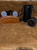 Kofu 7X35 binoculars with tan leather carrying case and Solinger lens with black case on brown surface.