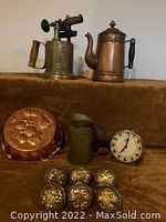 Photo showing Turner 150 blow torch, copper-finish coffee pot, copper fruit baking mold, metal jug, clock, and six brass door knobs arranged on a surface.