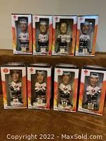 Eight hockey player bobble heads each in its original box with clear plastic display front, arranged in two rows of four on carpeted floor.