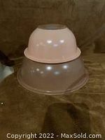 Two stacked peach colored Pyrex bowls showing their shape and size difference.