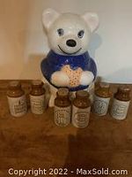 White ceramic polarbear cookie jar holding a gingerbread man in a blue sweater with six miniature spice crocks in front.