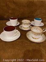 Front view of 5 assorted cups and saucers showing different colors and gold ornate decoration.