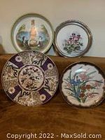 Front view of two Imari plates and three trays showing various floral, geometric, and advertising designs.