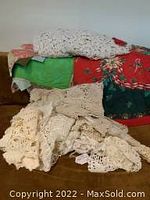 Pile of assorted crocheted linens including tablecloths, runners, and doilies in cream/off-white color.