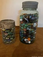 Two glass jars filled with assorted colorful marbles, one larger and one smaller jar, both sealed with metal lids.