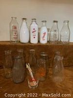 Front view of assorted vintage milk bottles showing various logos and conditions.