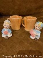 Front view of two orange Fire King mugs and two small Japanese figurines holding hearts, placed on brown surface
