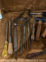 Various old hand tools arranged on brown cloth including files, pry bars, hammers, and chisels.