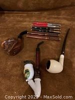 Four unique smoking pipes including German hand-painted, porcelain bowl, carved head and bent stem pipes along with five pens.