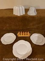 Two white jelly molds, three white scalloped plates, and one drip glaze toast rack on a brown surface