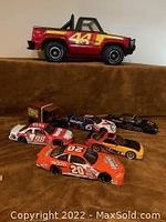 Photo showing one Tonka pressed steel Bronco 4x4 truck and seven metal advertising race cars arranged in rows on a brown fabric surface.