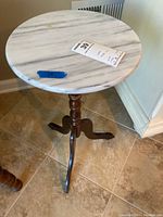 Round white marble top corner table with turned wood tripod base, placed on tiled floor near wall.